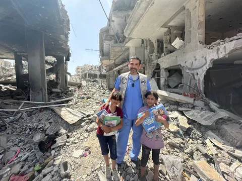 El Dr. Hamawy con dos niñas que sostienen útiles escolares entre edificios destruidos en Gaza