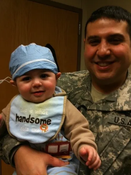 El teniente coronel Hamawy, con su uniforme del Ejército, sostiene a un bebé sonriente con gorro quirúrgico