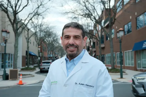 El Dr. Hamawy sonríe con una bata blanca de médico con su nombre bordado